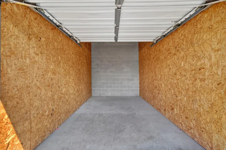Enclosed storage unit featuring a concrete floor, composite wood paneling, and a block wall