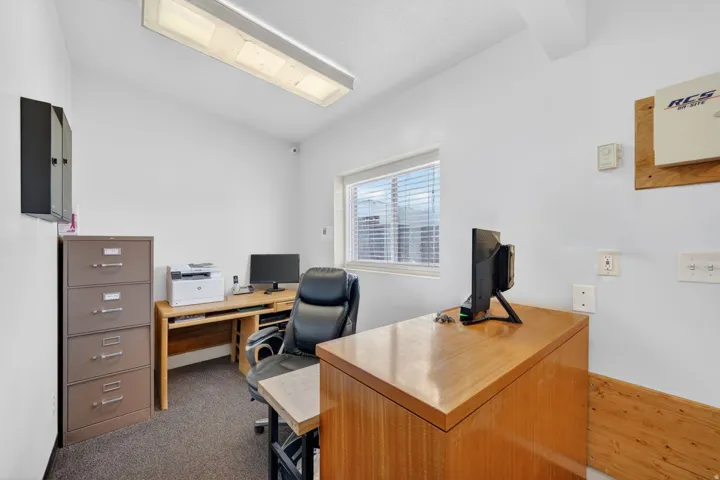 Interior space featuring a window with horizontal blinds, overhead fluorescent lighting, and wall-mounted electrical outlets