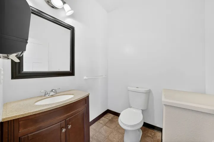 Bathroom featuring a dark wood-finish vanity with an integrated sink, a light-colored countertop, and a framed mirror