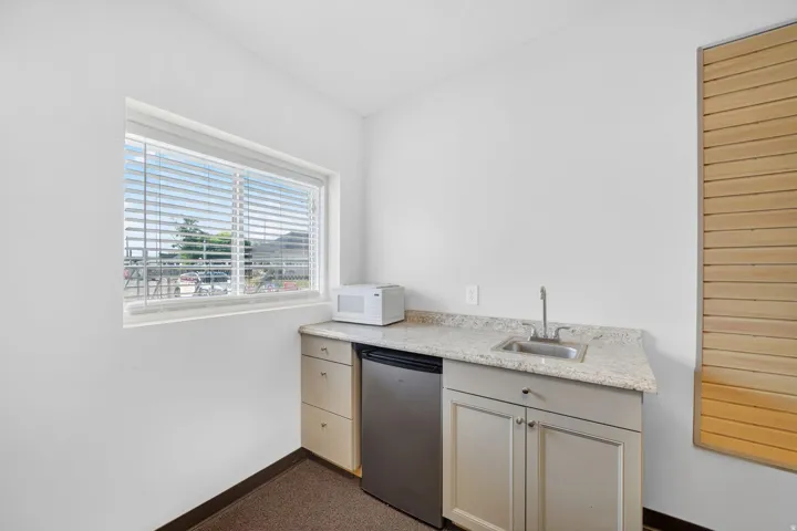 Compact kitchenette featuring a built-in stainless steel sink, light-toned countertop, and white cabinetry