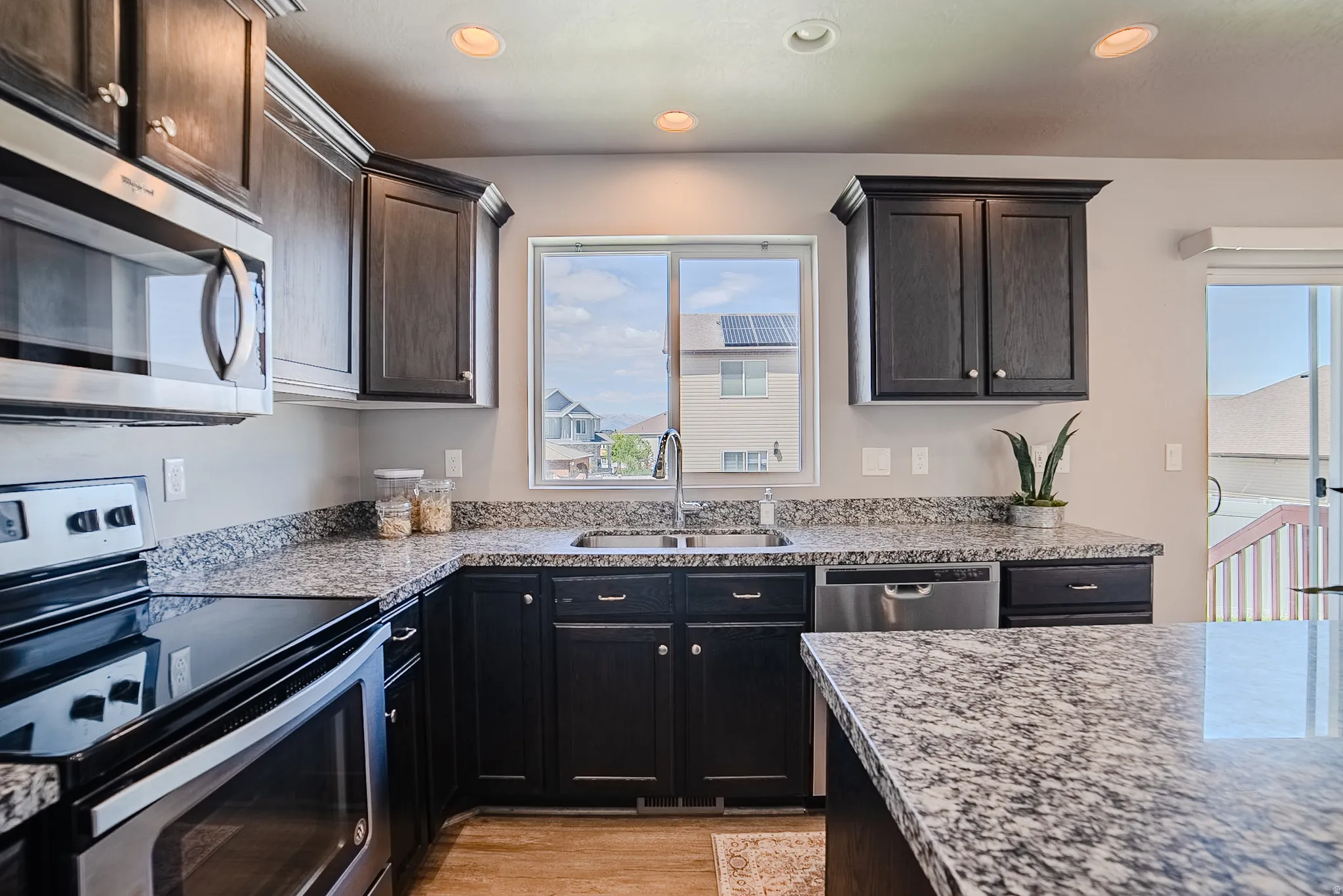 Kitchen featuring dark wood cabinetry, stainless steel appliances, speckled stone countertops, and recessed lighting