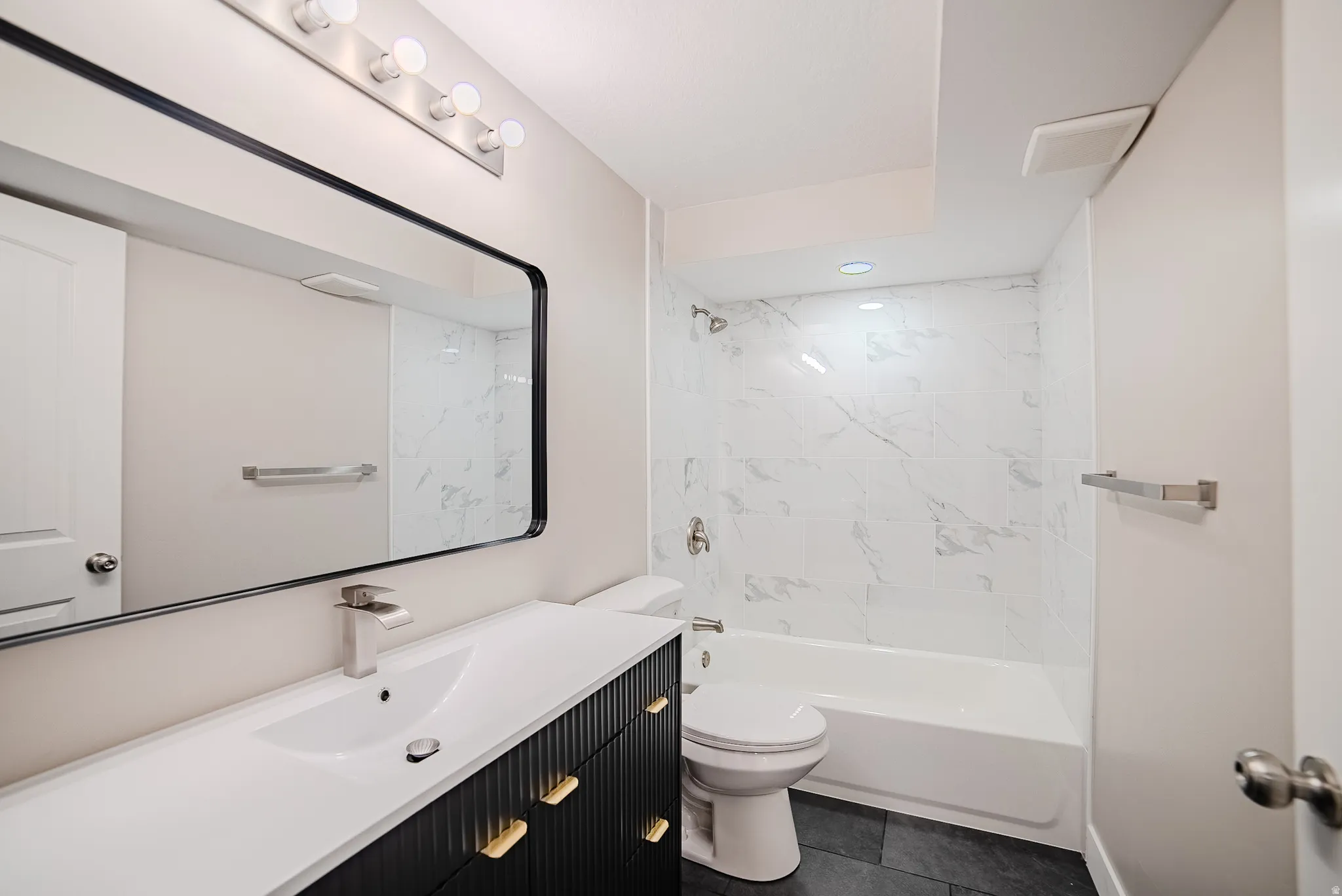 Contemporary bathroom featuring a black vanity with gold hardware, a white integrated sink, and a framed rectangular mirror