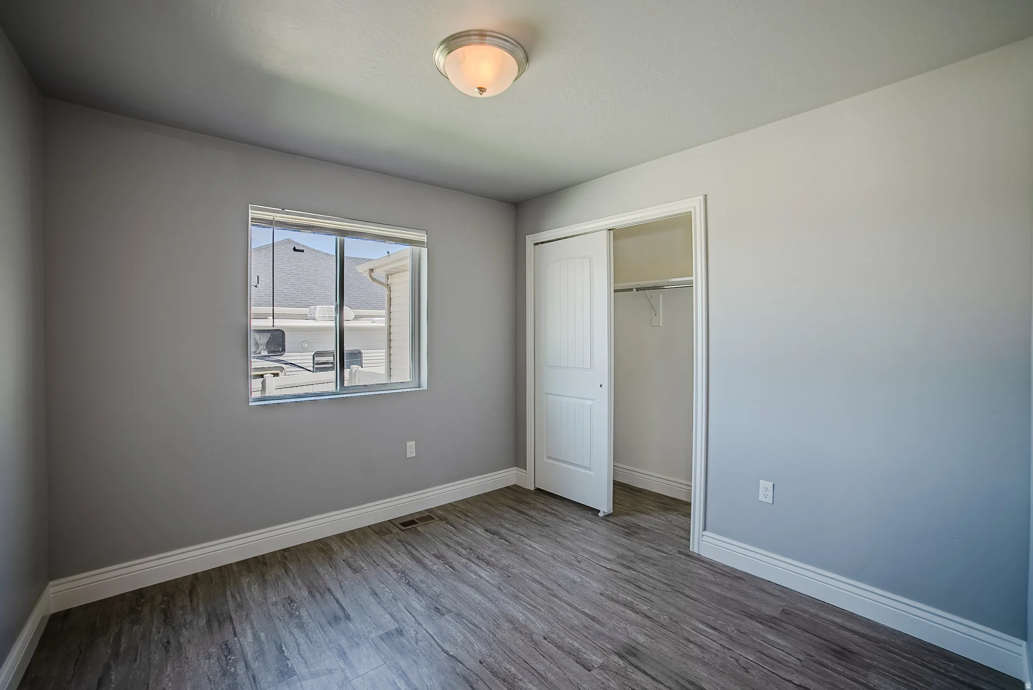 Room featuring wood-finish flooring, neutral gray walls, white trim, a double-paned window, and a built-in closet with sliding doors