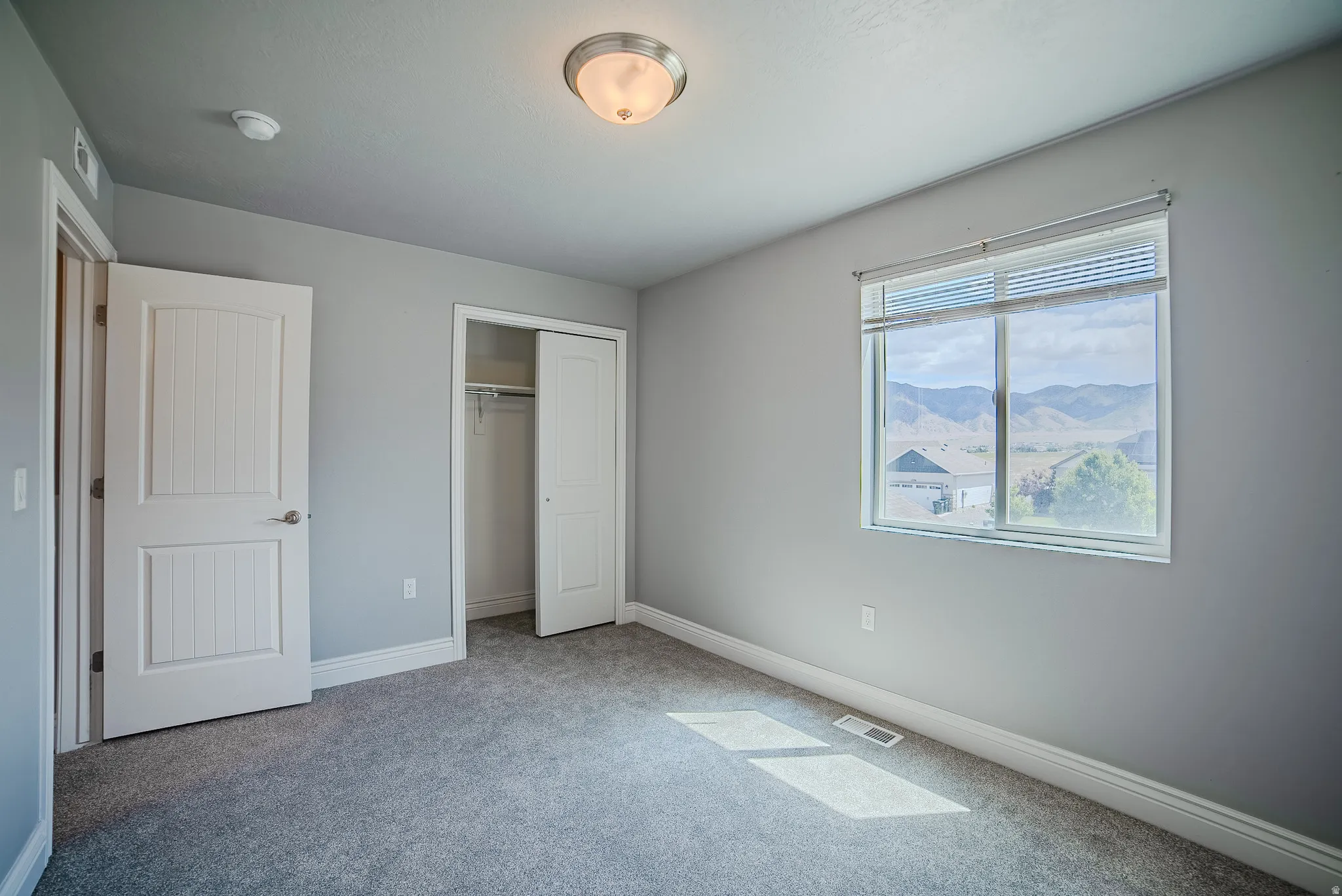 Carpeted room featuring a large window with blinds, a flush-mount ceiling light, a white paneled door, and a bi-fold closet door