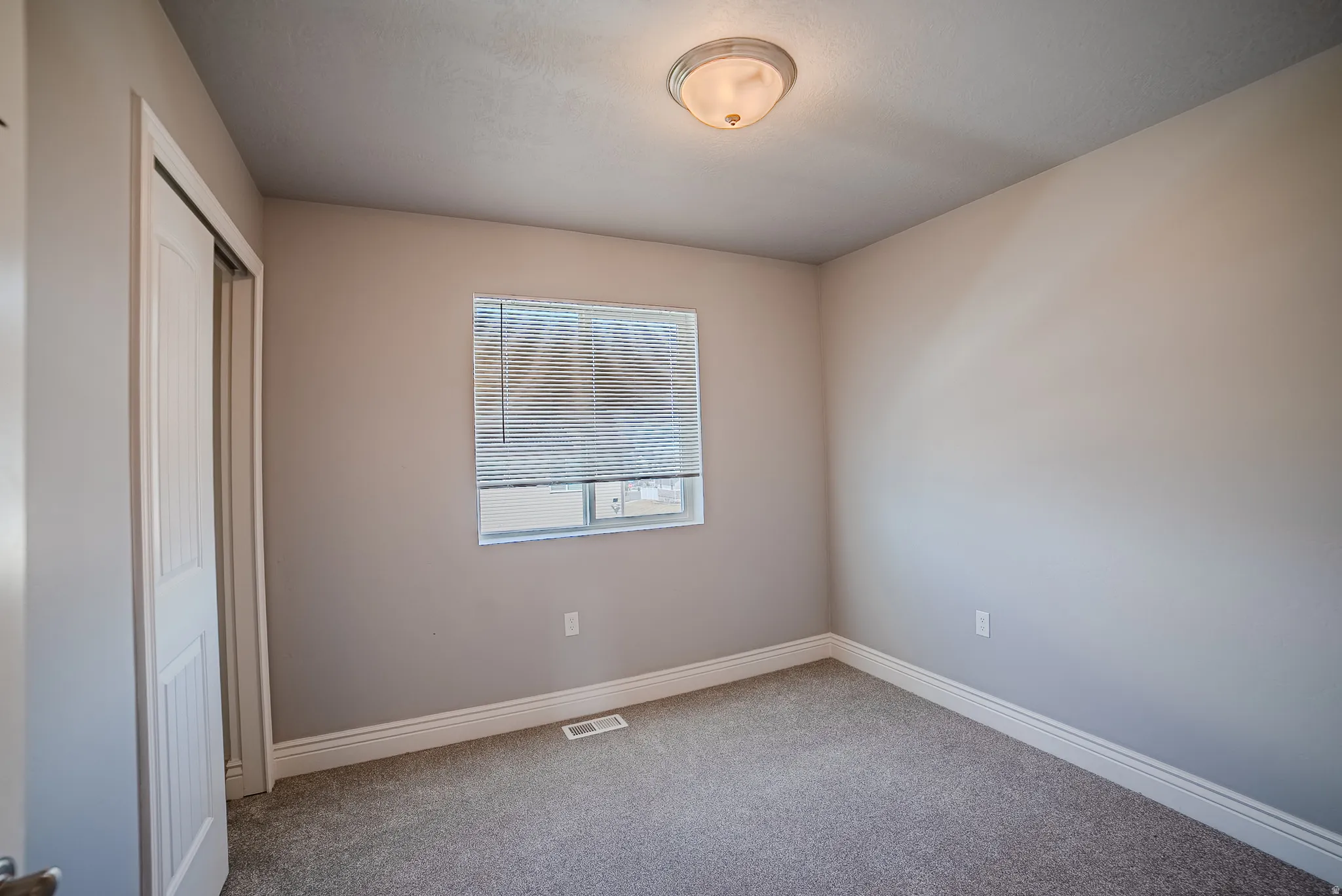 Carpeted room featuring a window with horizontal blinds, a flush mount ceiling light fixture, bi-fold closet doors, and white baseboards