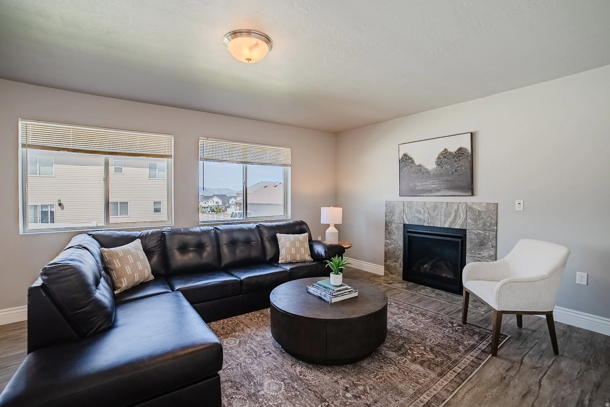 Living area featuring a fireplace with a stone tile surround, wood-finish flooring, two windows with blinds, and a semi-flush mount ceiling light