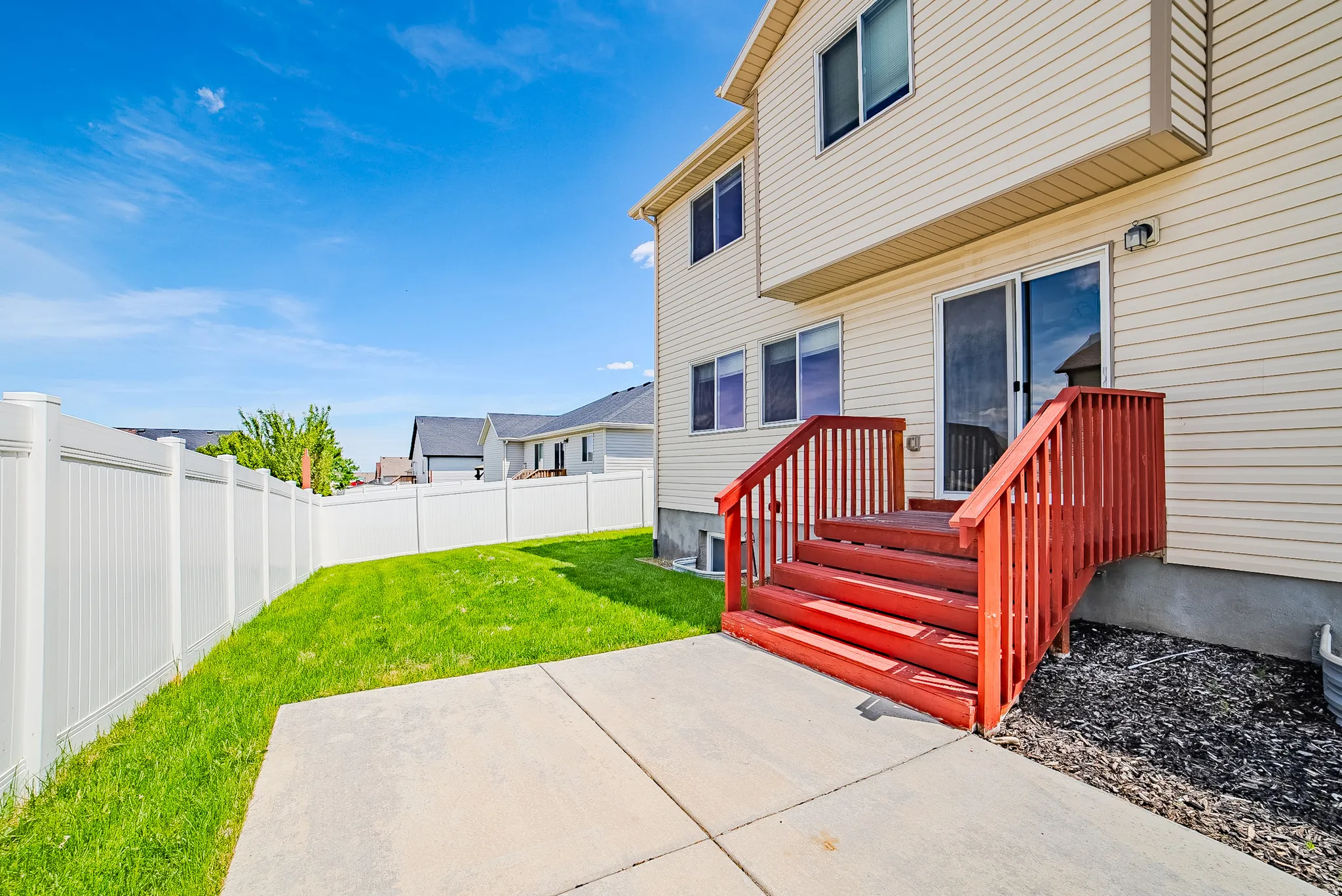 Rear exterior featuring a concrete patio, red-stained wooden stairs, and a sliding glass door