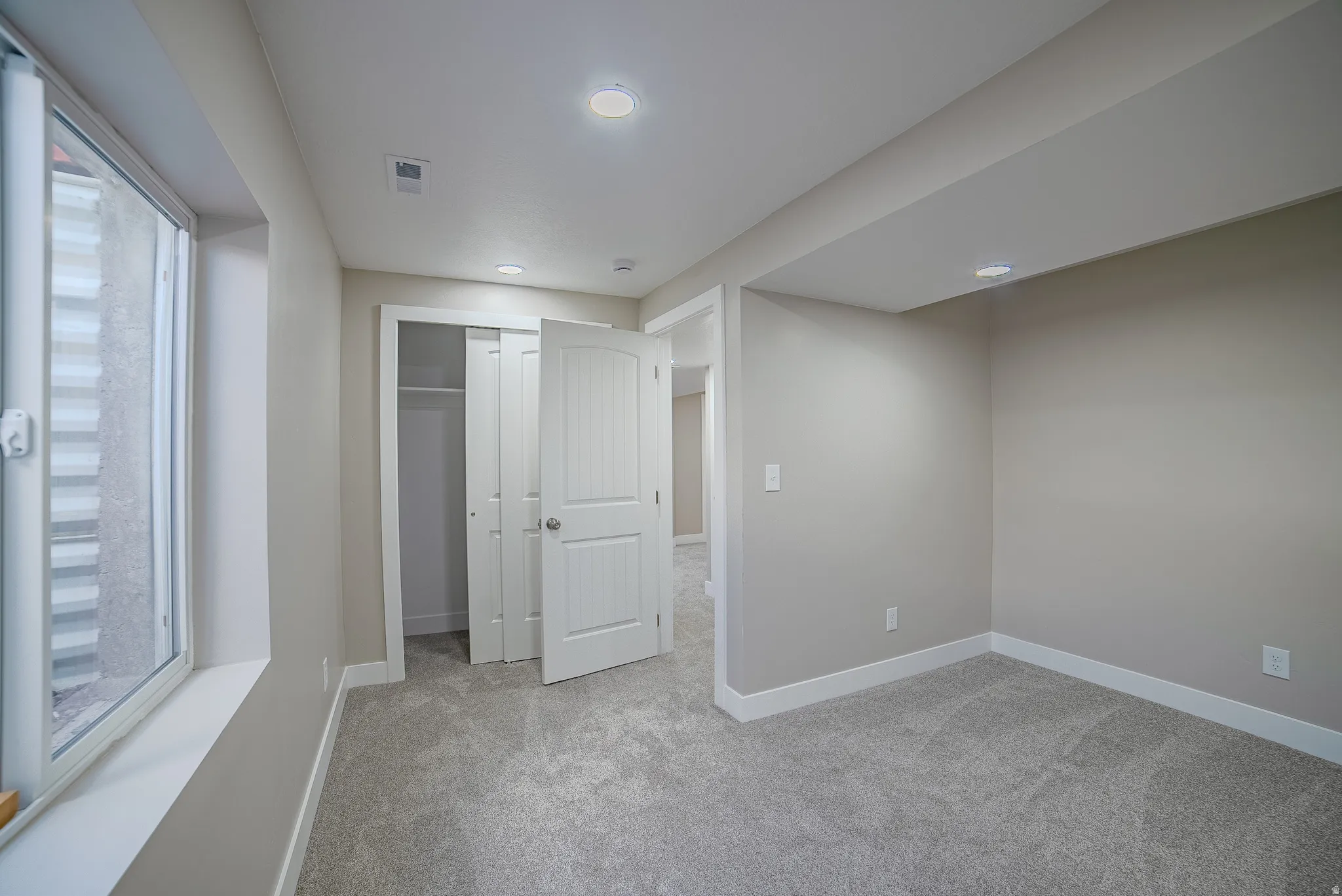 Room featuring light gray carpet, recessed lighting, a window with a white frame and window well, white baseboards, and a closet with bifold doors