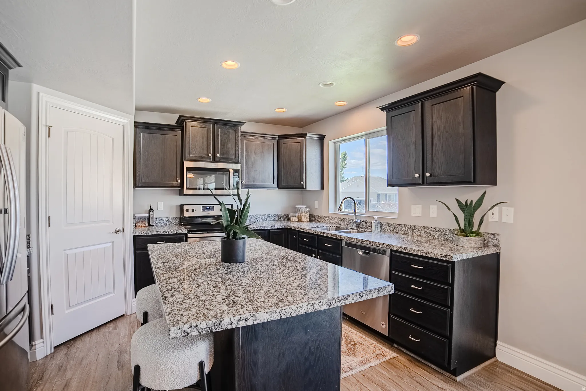 Modern kitchen featuring dark wood-finish cabinetry, speckled countertops, stainless steel appliances, and wood-finish flooring