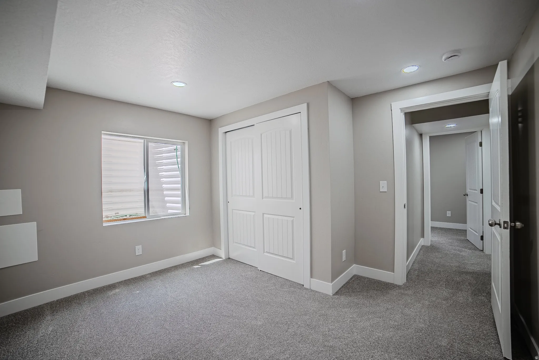 Carpeted room featuring a white bi-fold closet, recessed ceiling lighting, a window with horizontal blinds, and a neutral wall color