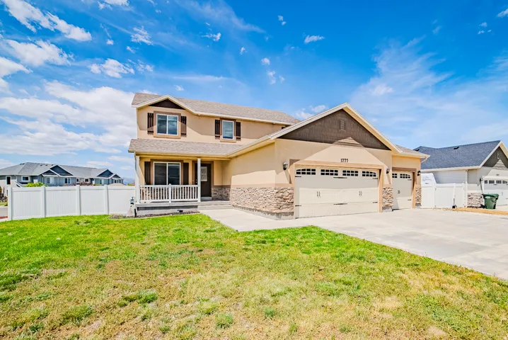 Two-story stucco exterior with stone accents, featuring a covered front porch with white railings, a three-car garage, and an expansive concrete driveway