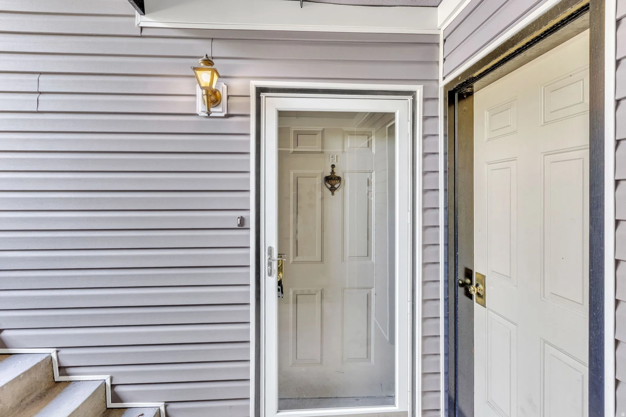 Entryway featuring a white paneled door with a brass knocker, a white storm door, and a brass wall-mounted light fixture