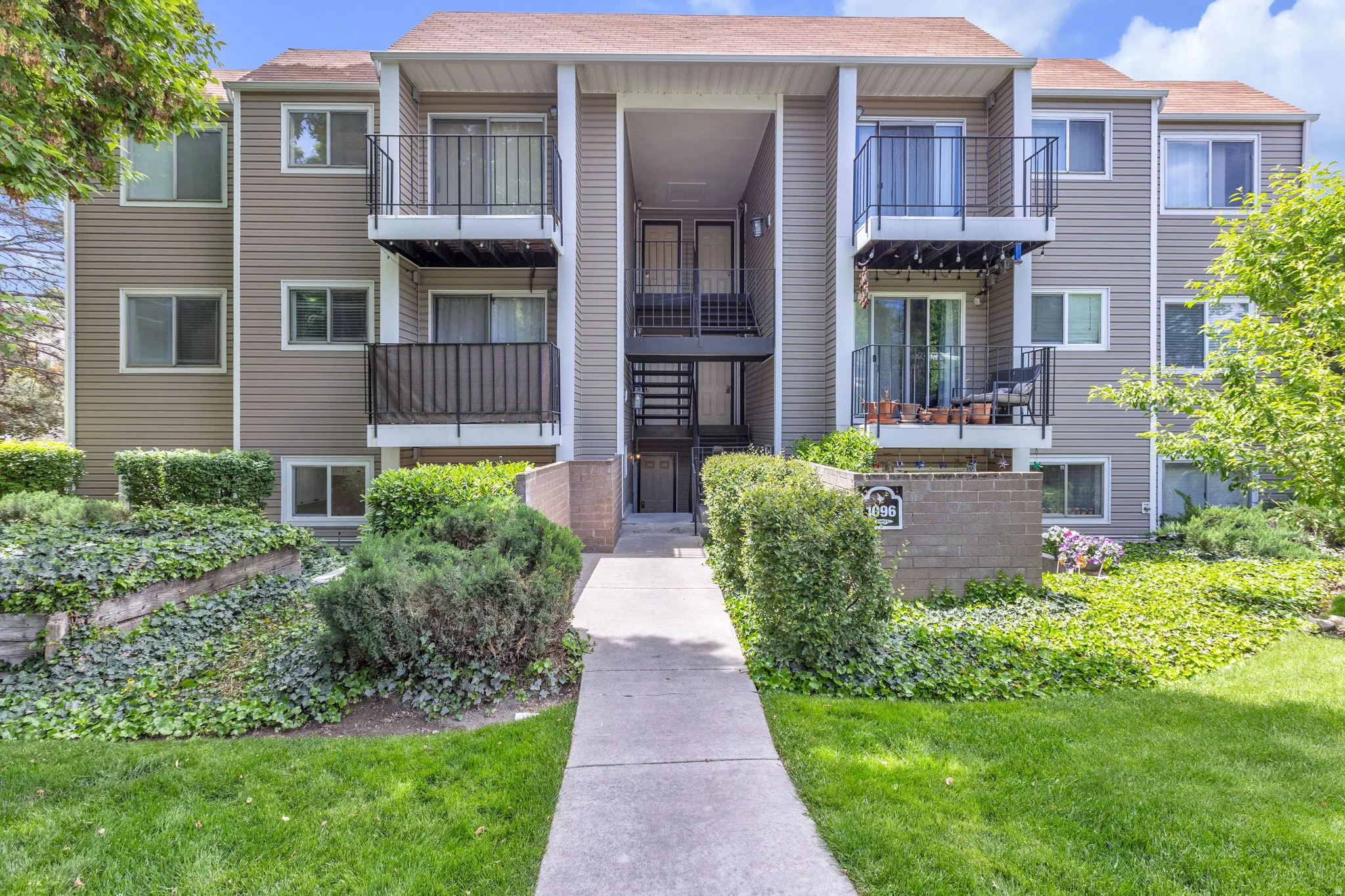 Multi-story residential building featuring balconies with black metal railings, neutral-toned siding, and a gabled roofline
