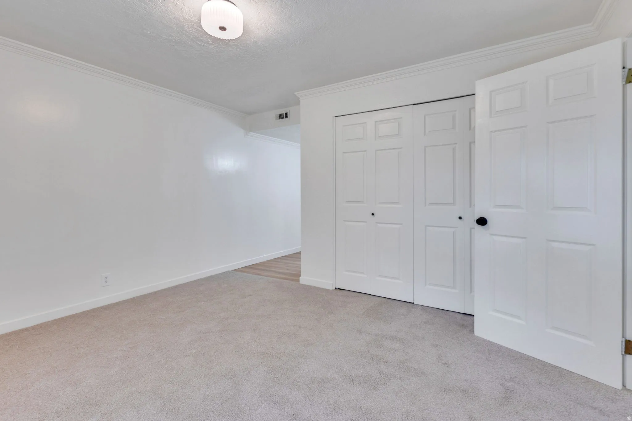Neutral tone carpeting in a room featuring white walls and crown molding
