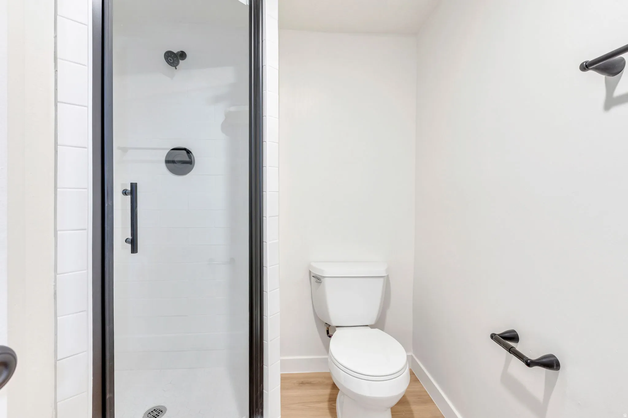 Shower enclosure with clear glass door and black framing, featuring a matte black shower head and handle