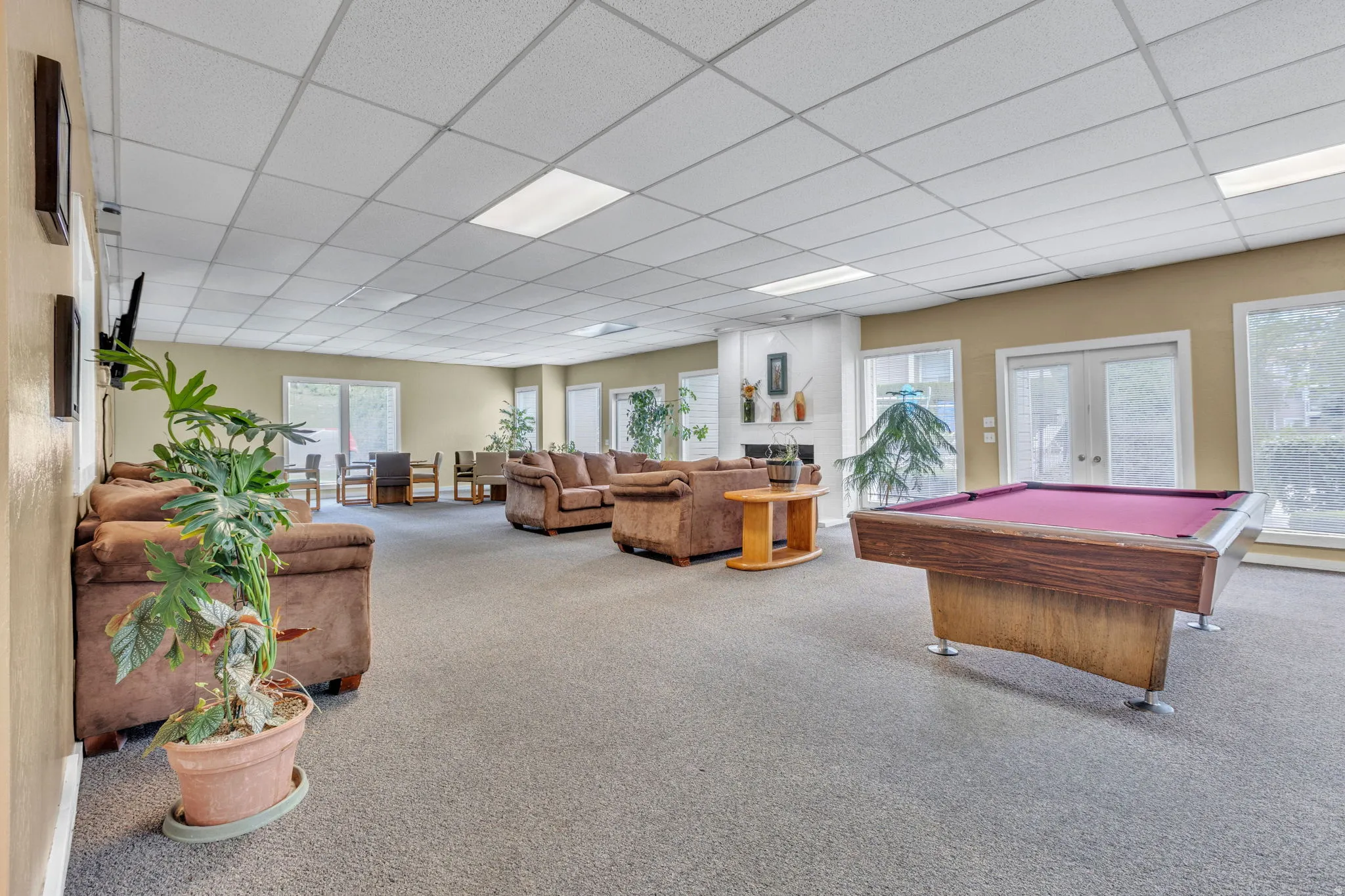 Spacious common room featuring carpeted flooring and an acoustic tile ceiling with integrated lighting