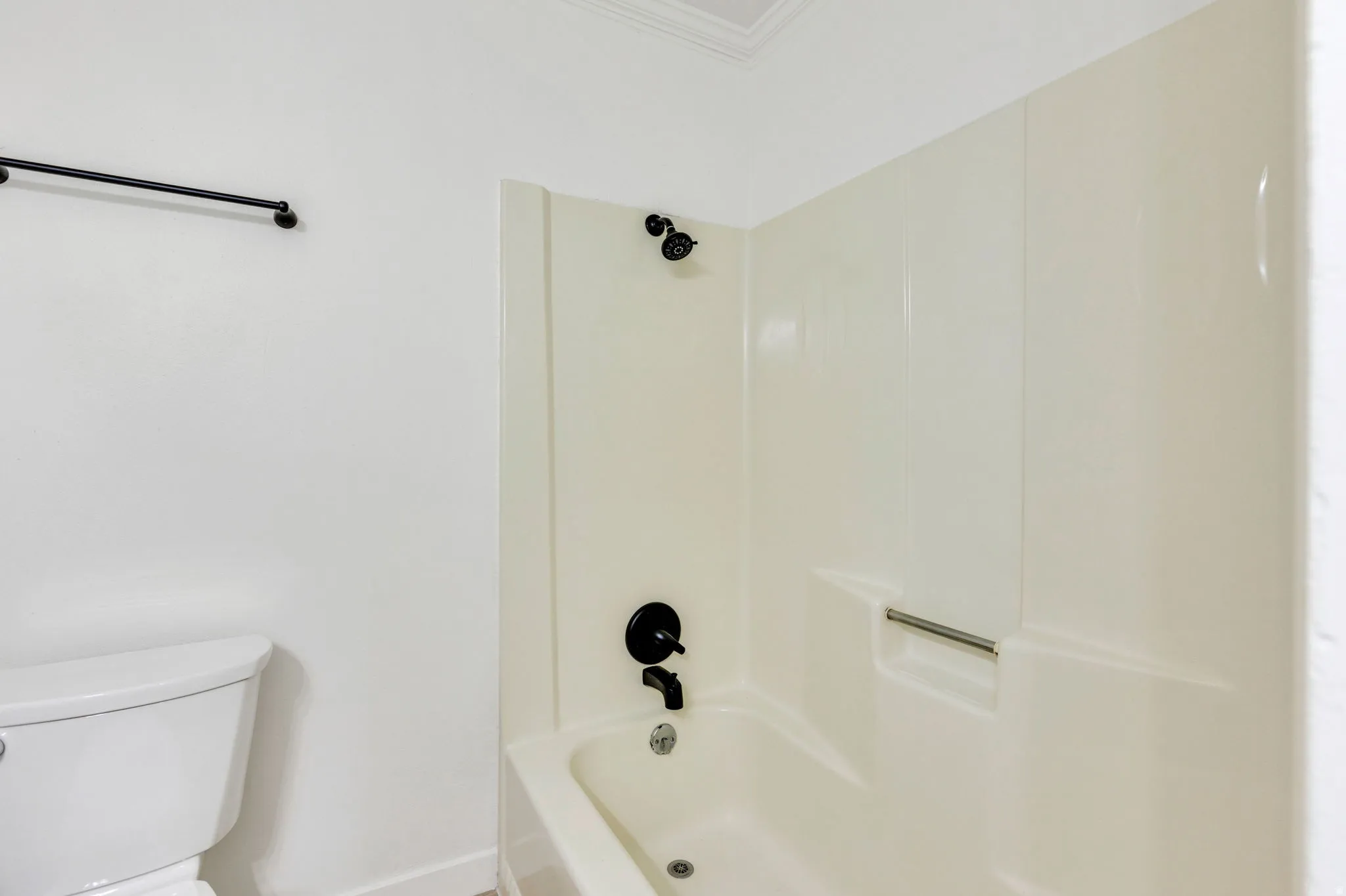 Bathtub and shower combination with dark bronze fixtures and a white acrylic surround