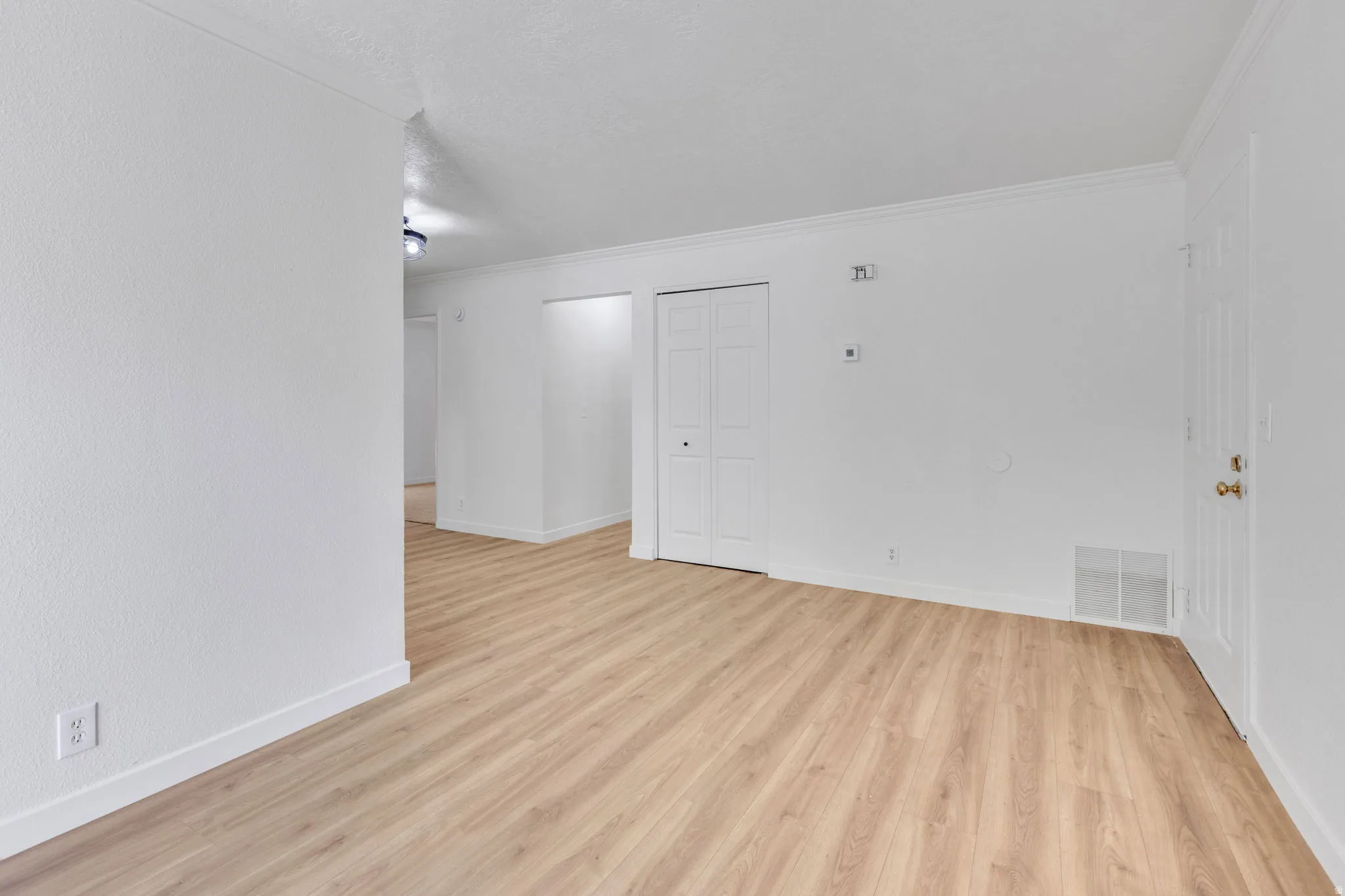 Open living area featuring wood-finish flooring, white baseboards, and crown molding
