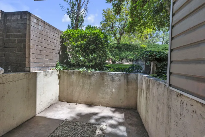 Enclosed concrete patio area with a brick retaining wall and mature landscaping