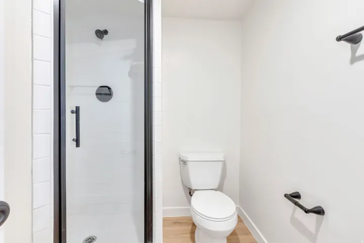 Shower enclosure with clear glass door and black framing, featuring a matte black shower head and handle