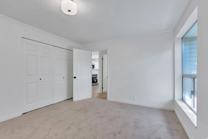 Carpeted room with white paneled bifold closet doors, a single window, and a drum-style ceiling light fixture