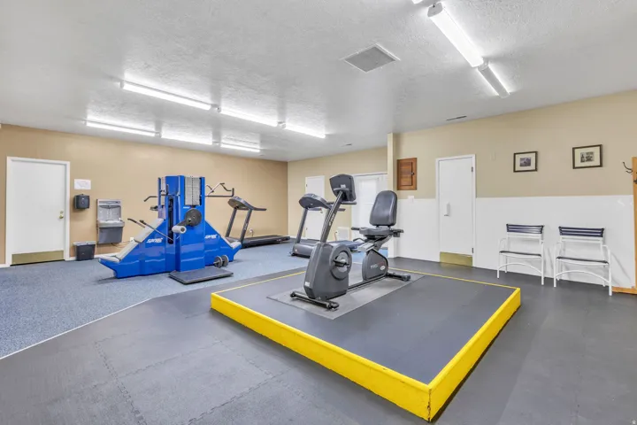 Dedicated fitness area featuring durable rubber flooring, a raised exercise platform, recessed ceiling lighting, and a beige and white wall palette