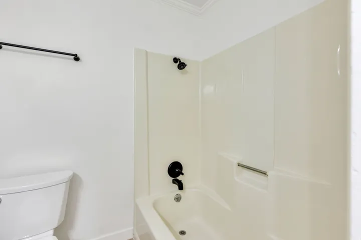 Bathtub and shower combination with dark bronze fixtures and a white acrylic surround