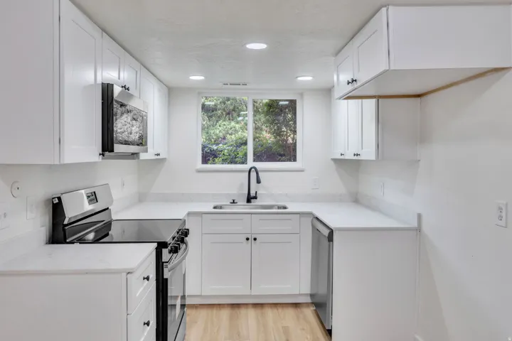 Kitchen featuring white cabinetry, light-toned countertops, a stainless steel electric range, an over-range microwave, and a black faucet