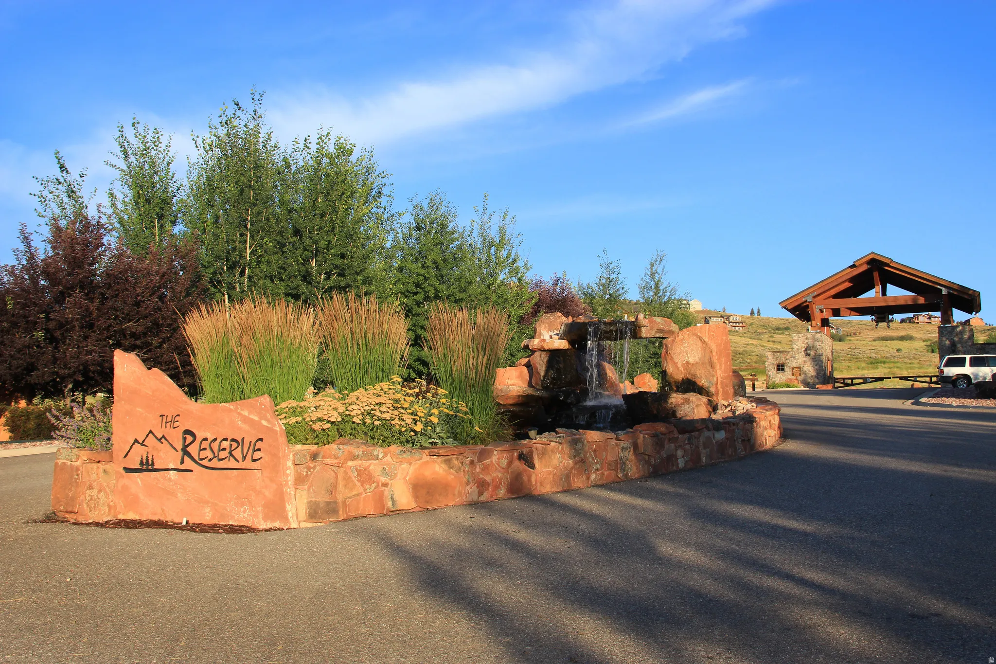 Stone entry monument with cascading water feature, diverse plantings, and a prominent community sign