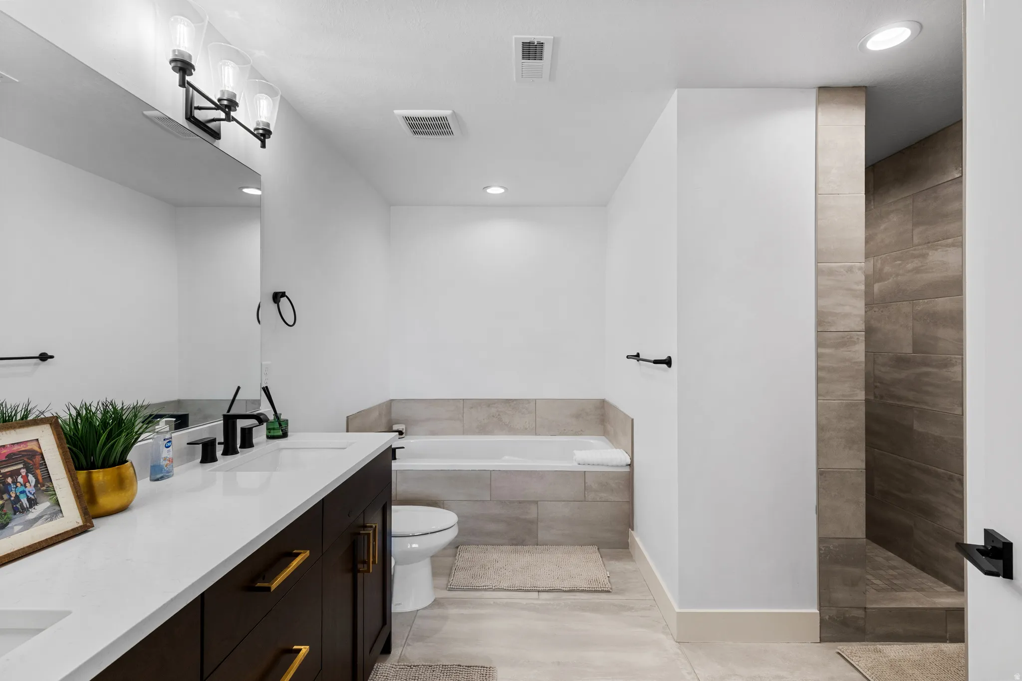 Contemporary bathroom featuring a dark wood-finish dual vanity with white countertops, matte black plumbing fixtures, and gold-tone hardware