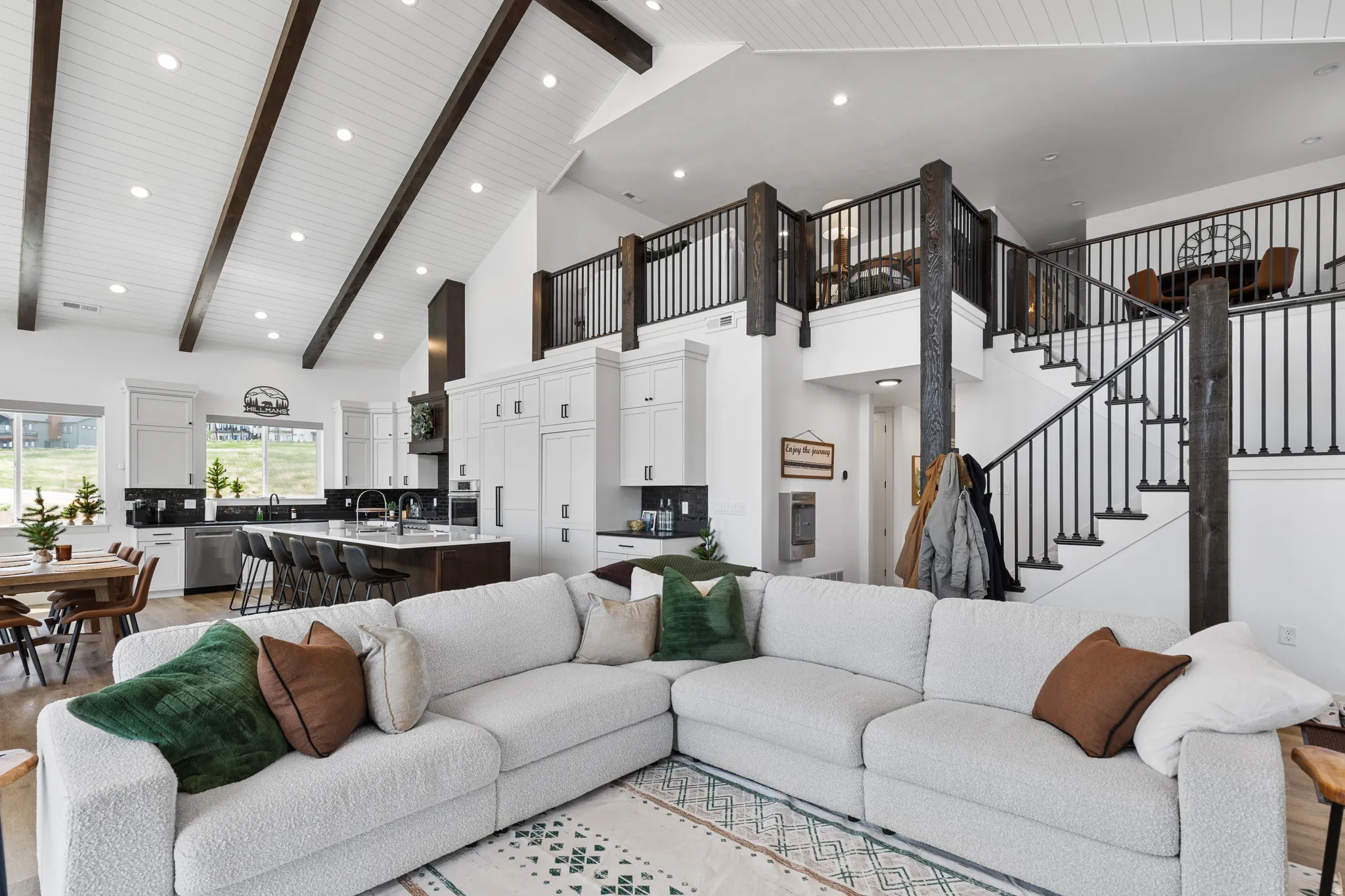 Vaulted ceiling with exposed wood beams, a spacious kitchen featuring an island with seating, stainless steel appliances, and wood-finish flooring