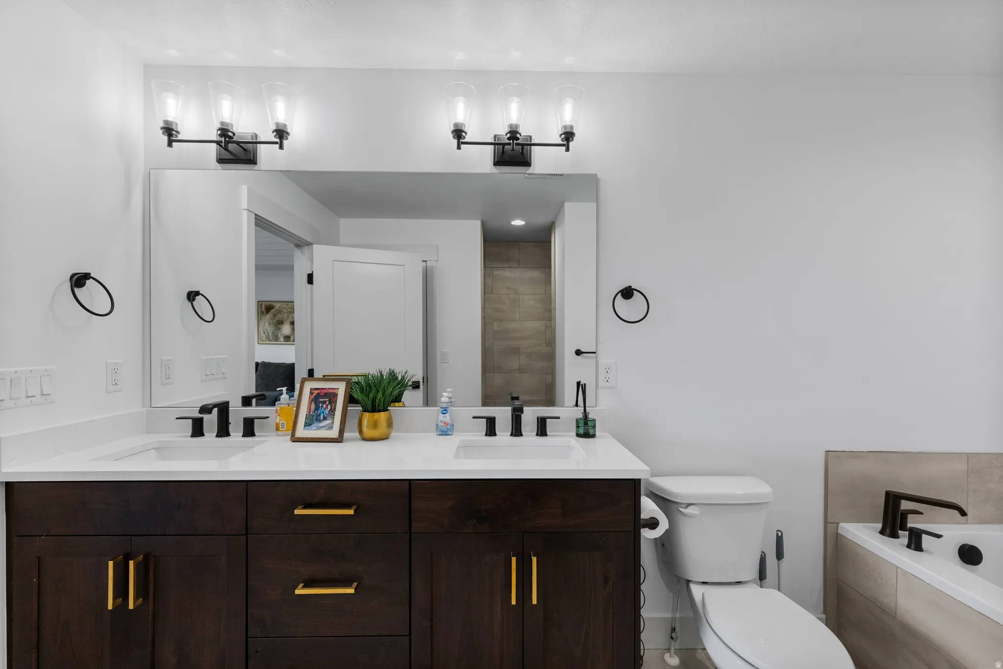 Double vanity featuring dark wood cabinetry with gold-finish hardware, undermount sinks, and white countertops