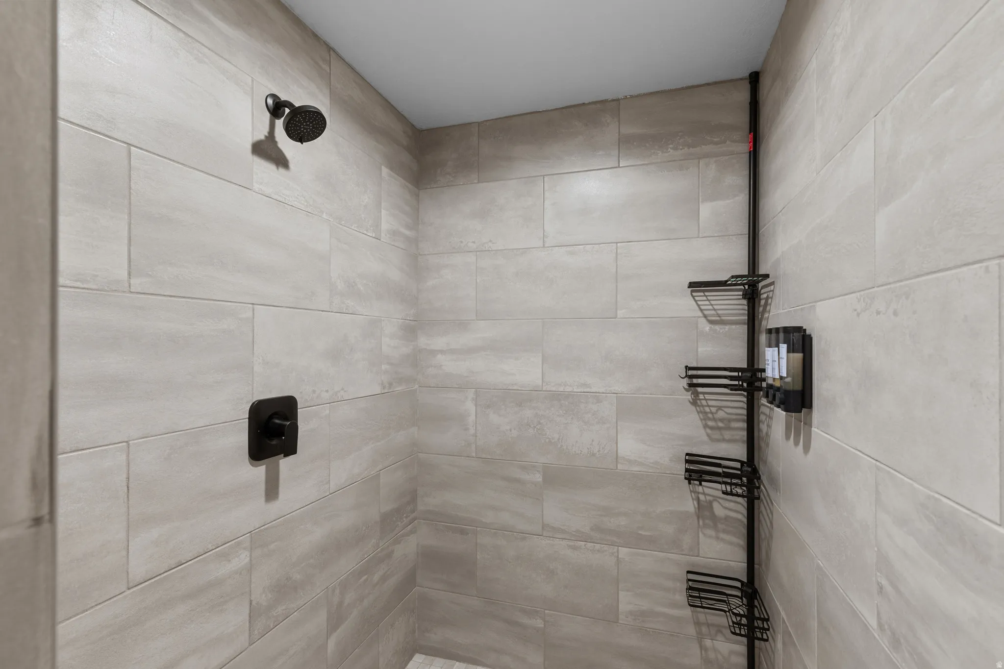 Shower enclosure featuring light-toned rectangular wall tiling, a matte black shower head, and a coordinating matte black control handle