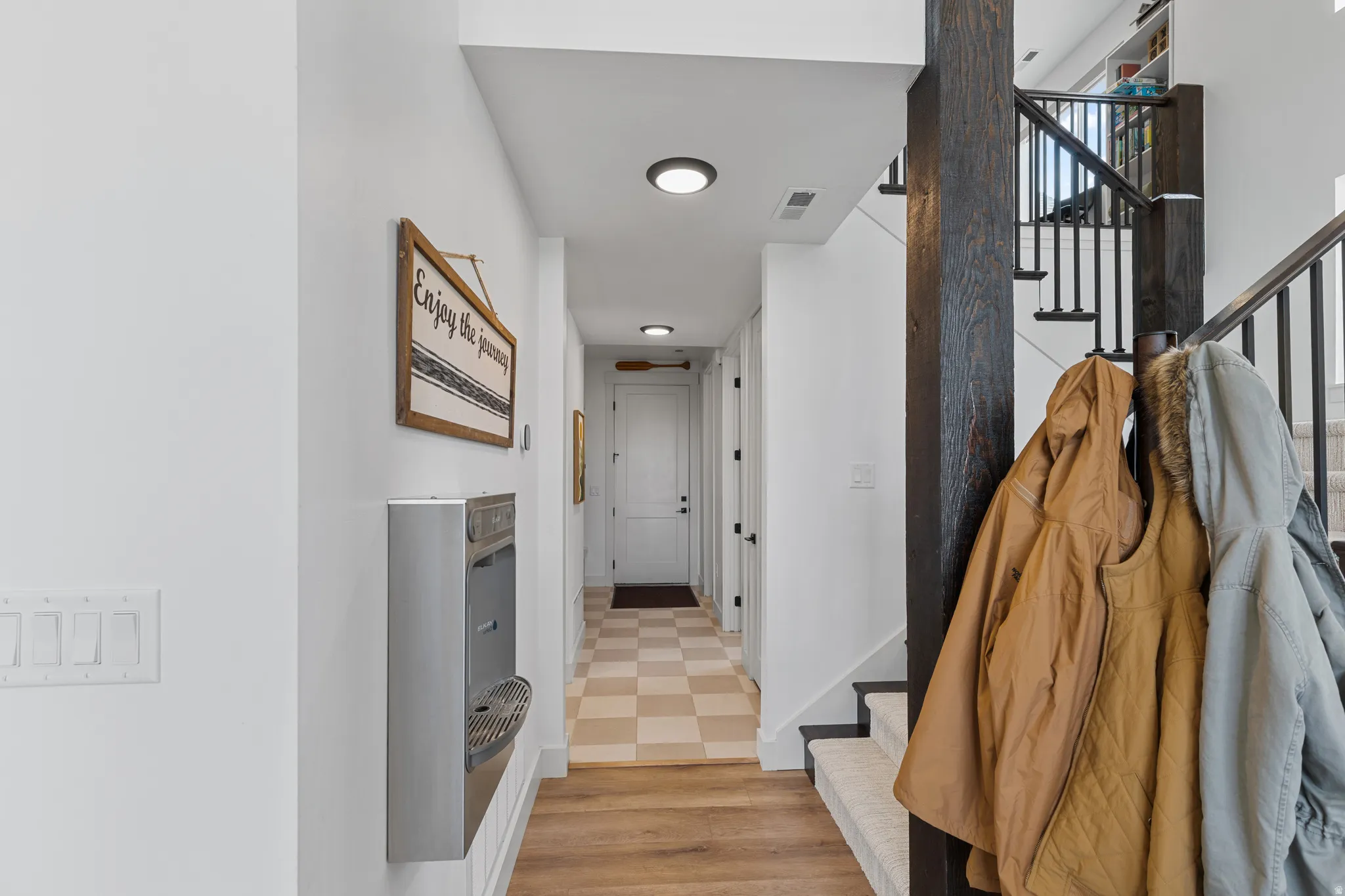 Hallway featuring wood-finish flooring, recessed lighting, and a staircase with black metal balusters and a dark wood newel post