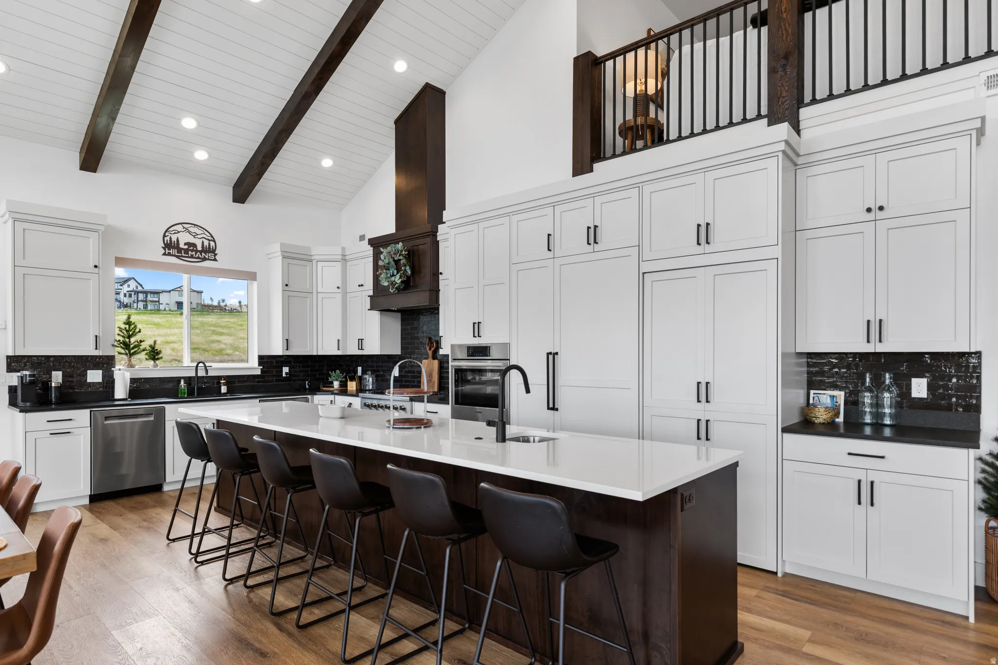 Spacious kitchen featuring an expansive center island with seating, a vaulted ceiling with exposed wood beams, and built-in stainless steel appliances