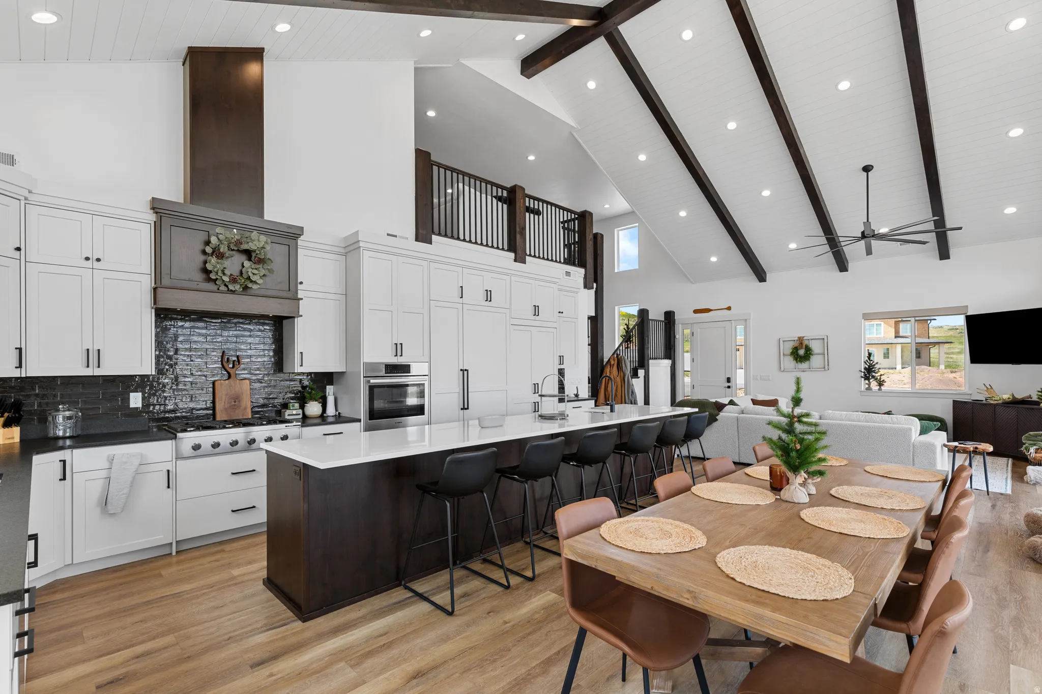 Expansive open-concept kitchen and living area featuring a vaulted ceiling with exposed dark wood beams and recessed lighting