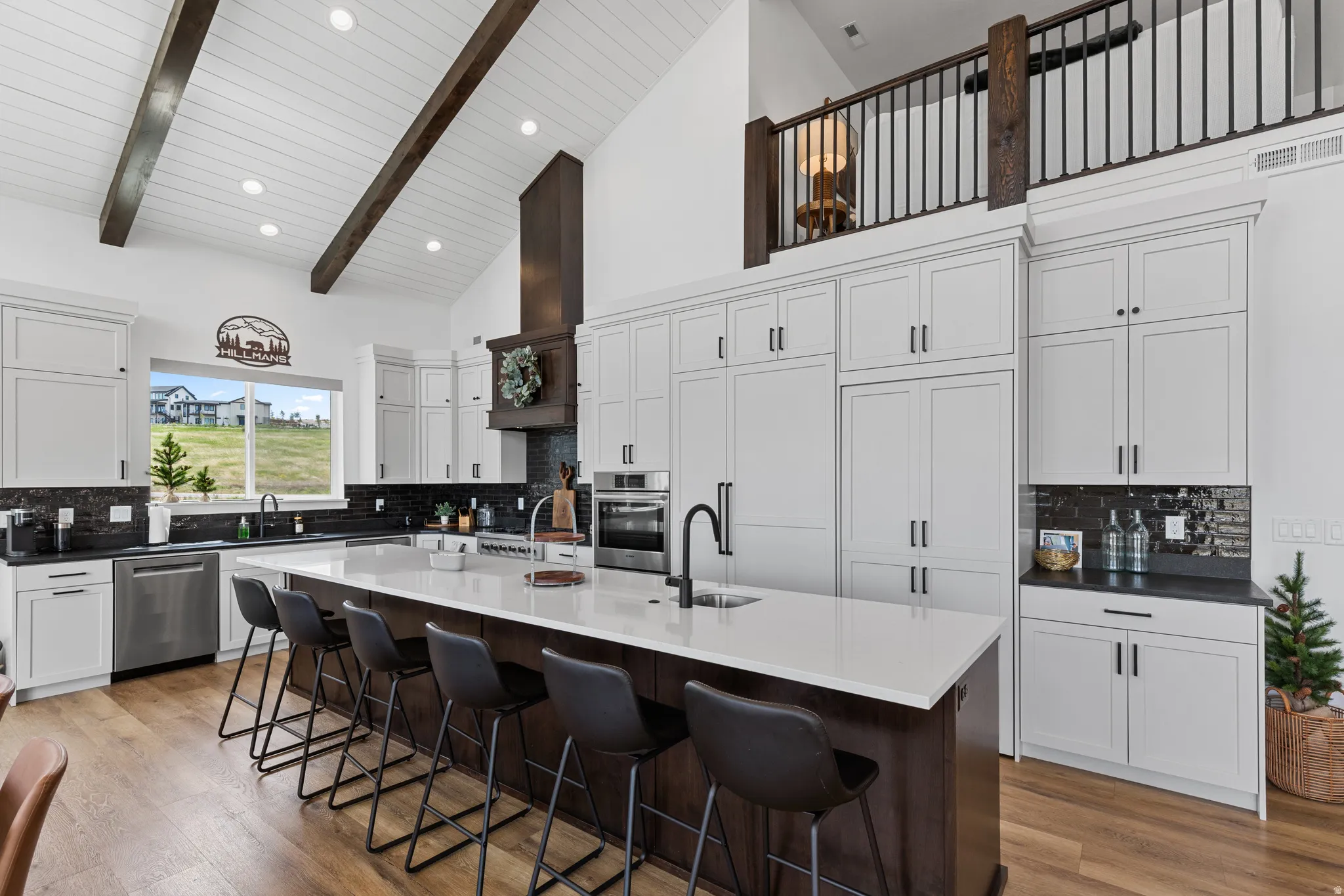 Spacious kitchen featuring an expansive central island with seating, a vaulted shiplap ceiling with exposed wood beams, extensive white cabinetry, and stainless steel appliances