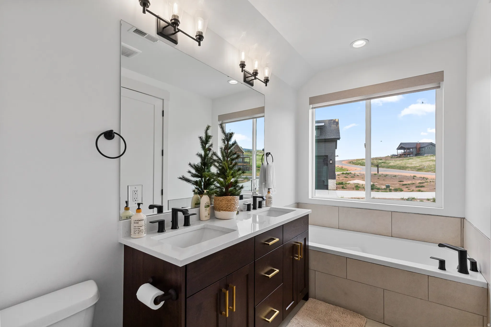 Dual sink vanity with dark wood-finish cabinetry, gold-tone hardware, and white countertops