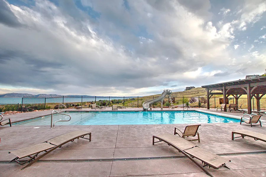 Outdoor swimming pool with a concrete surround, featuring a shallow wading area, an attached water slide, and a wooden pergola structure