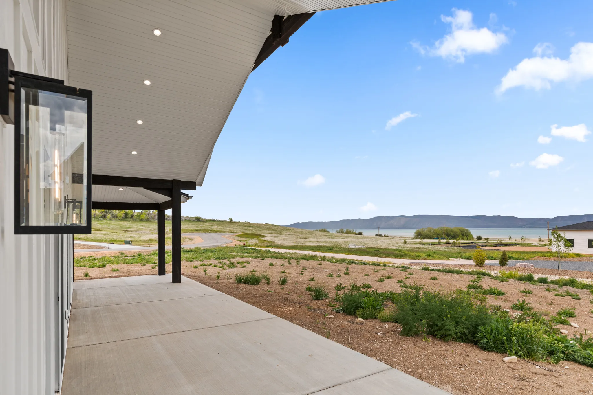 Covered patio with recessed lighting and a contemporary outdoor sconce, featuring a concrete surface and dark support columns