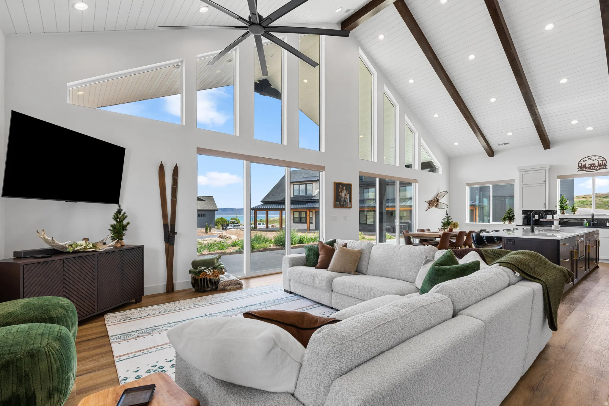 Open-concept living space featuring vaulted ceilings with exposed wood beams, wood-finish flooring, and expansive windows