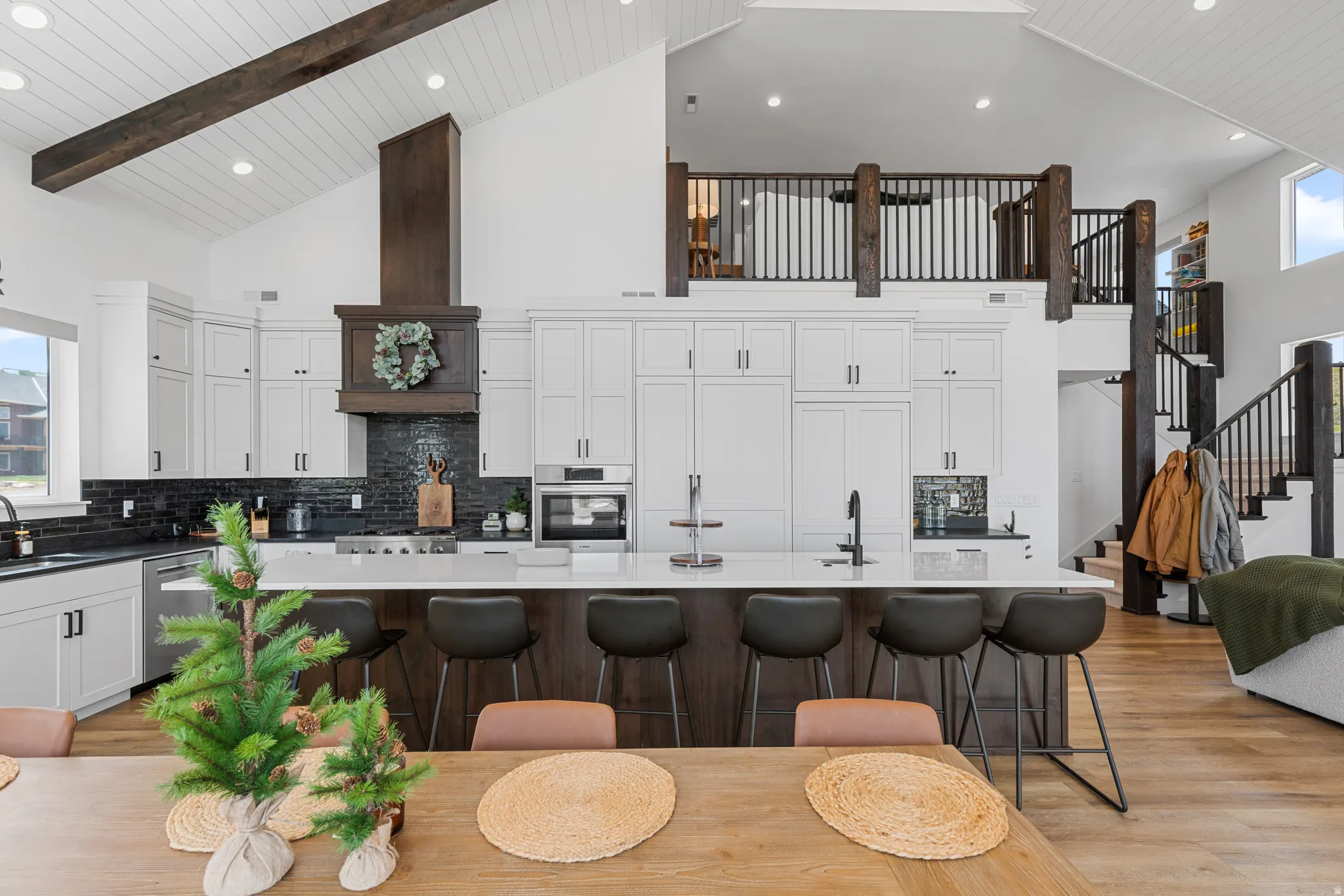 Open-concept kitchen featuring an oversized island with seating, dark wood-finish cabinetry, white upper cabinetry, a custom range hood, and stainless steel appliances
