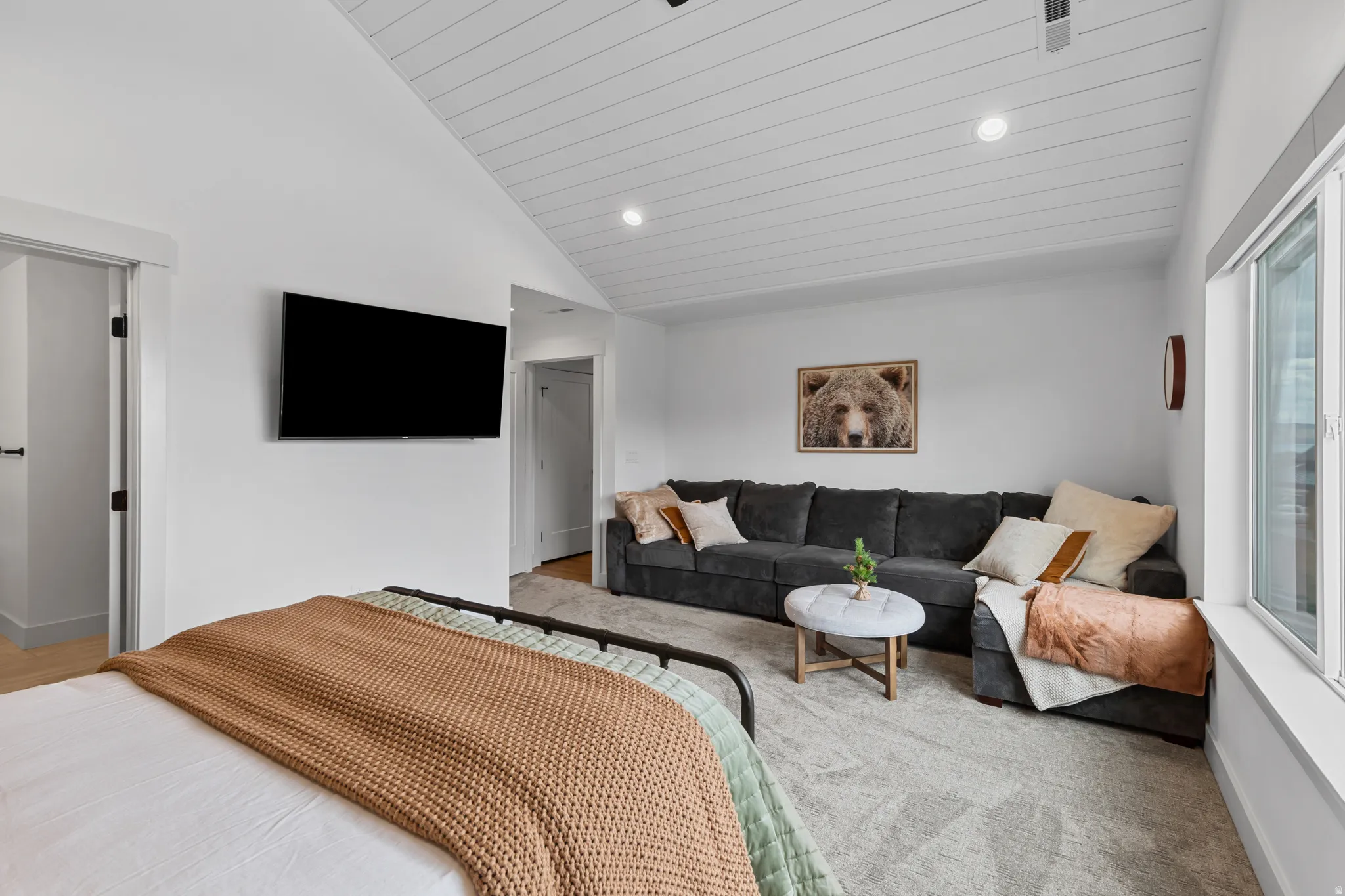 Vaulted ceiling with white shiplap finish, white walls, recessed lighting, and a large window