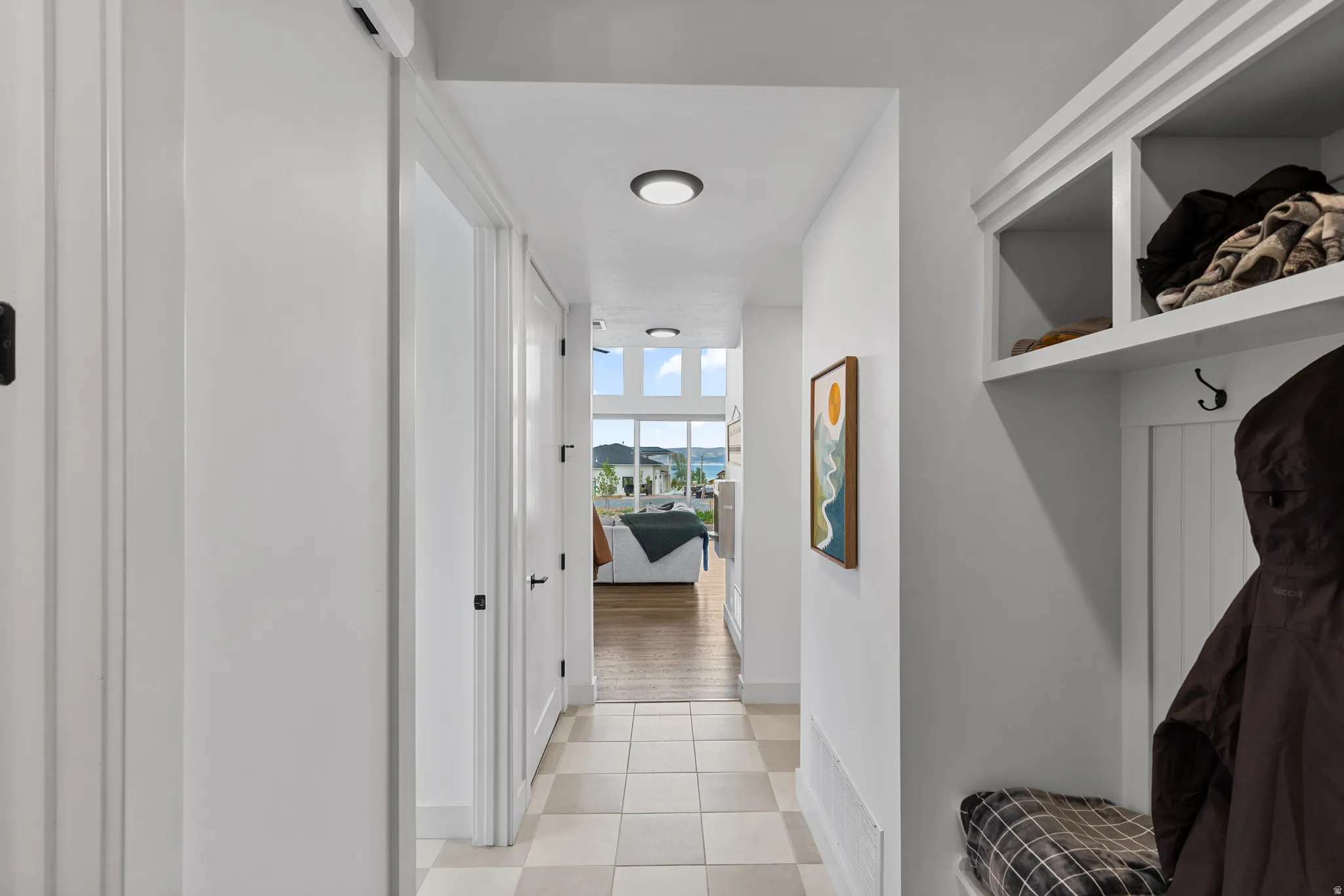 Hallway featuring light-toned square tile flooring, white walls, and a built-in storage bench with upper shelving and coat hooks