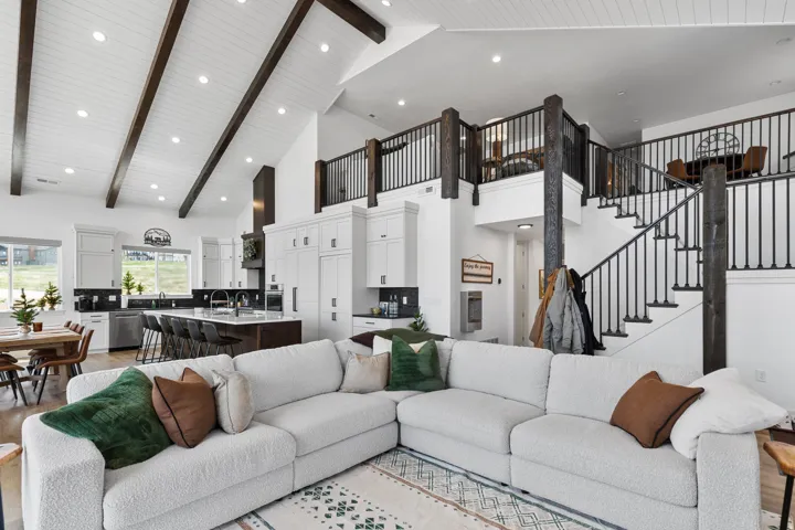 Vaulted ceiling with exposed wood beams, a spacious kitchen featuring an island with seating, stainless steel appliances, and wood-finish flooring