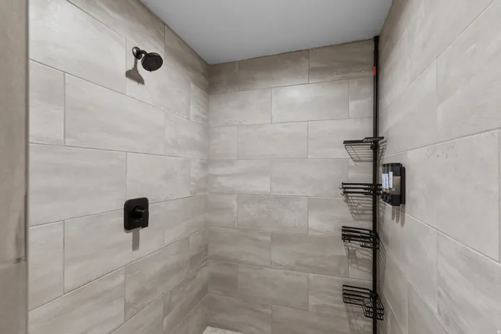 Shower enclosure featuring light-toned rectangular wall tiling, a matte black shower head, and a coordinating matte black control handle