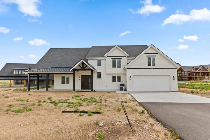 Contemporary farmhouse-style residence featuring white board-and-batten and horizontal siding, a dark shingle roof, an attached two-car garage with a concrete driveway, and a covered front entry with dark wood-toned columns and trim