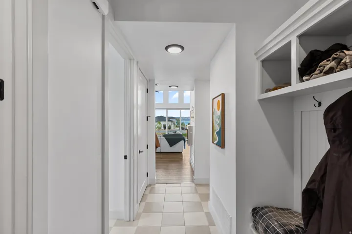 Hallway featuring light-toned square tile flooring, white walls, and a built-in storage bench with upper shelving and coat hooks