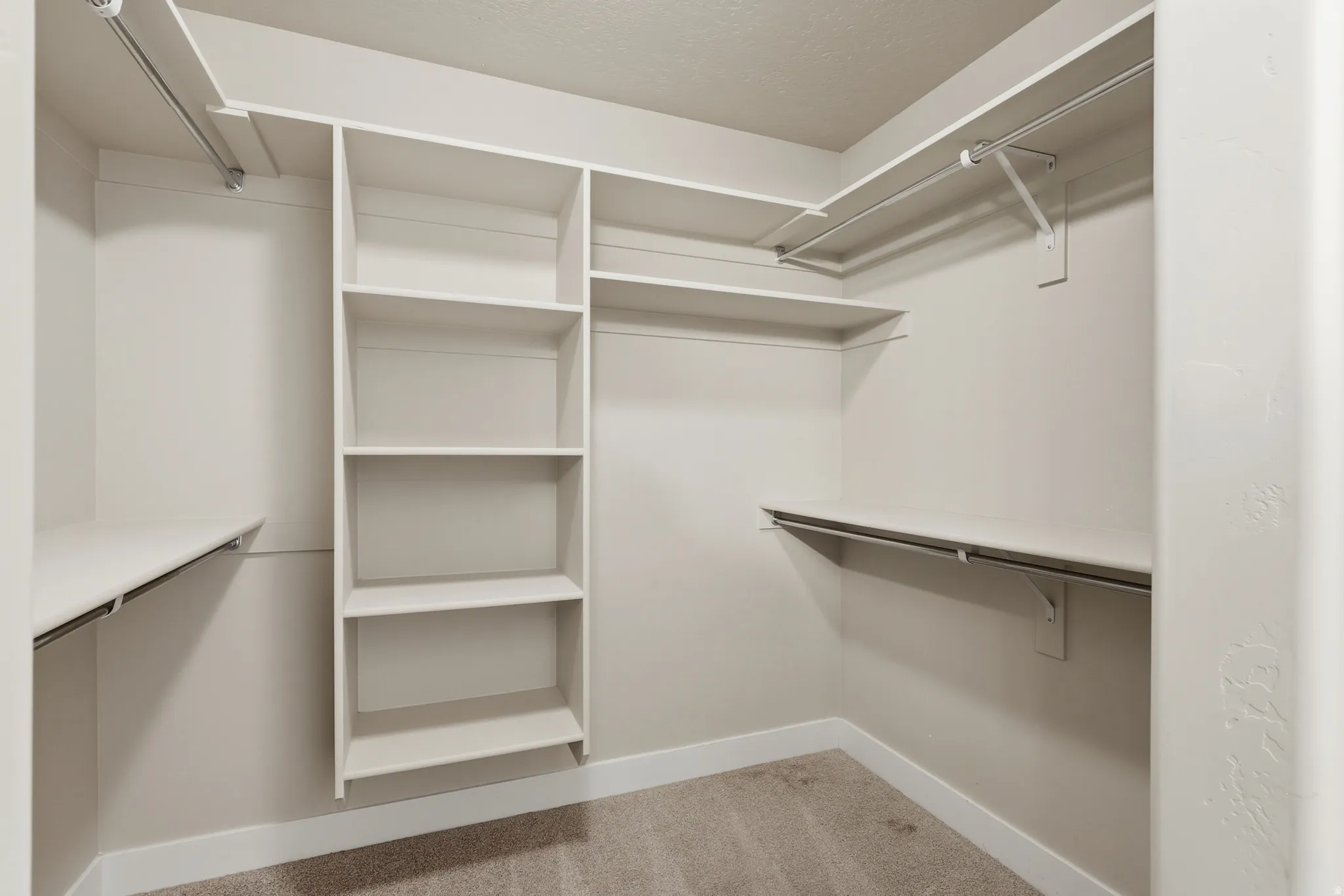 Spacious master suite walk-in closet featuring built-in shelving, multiple hanging rods, and neutral carpet flooring