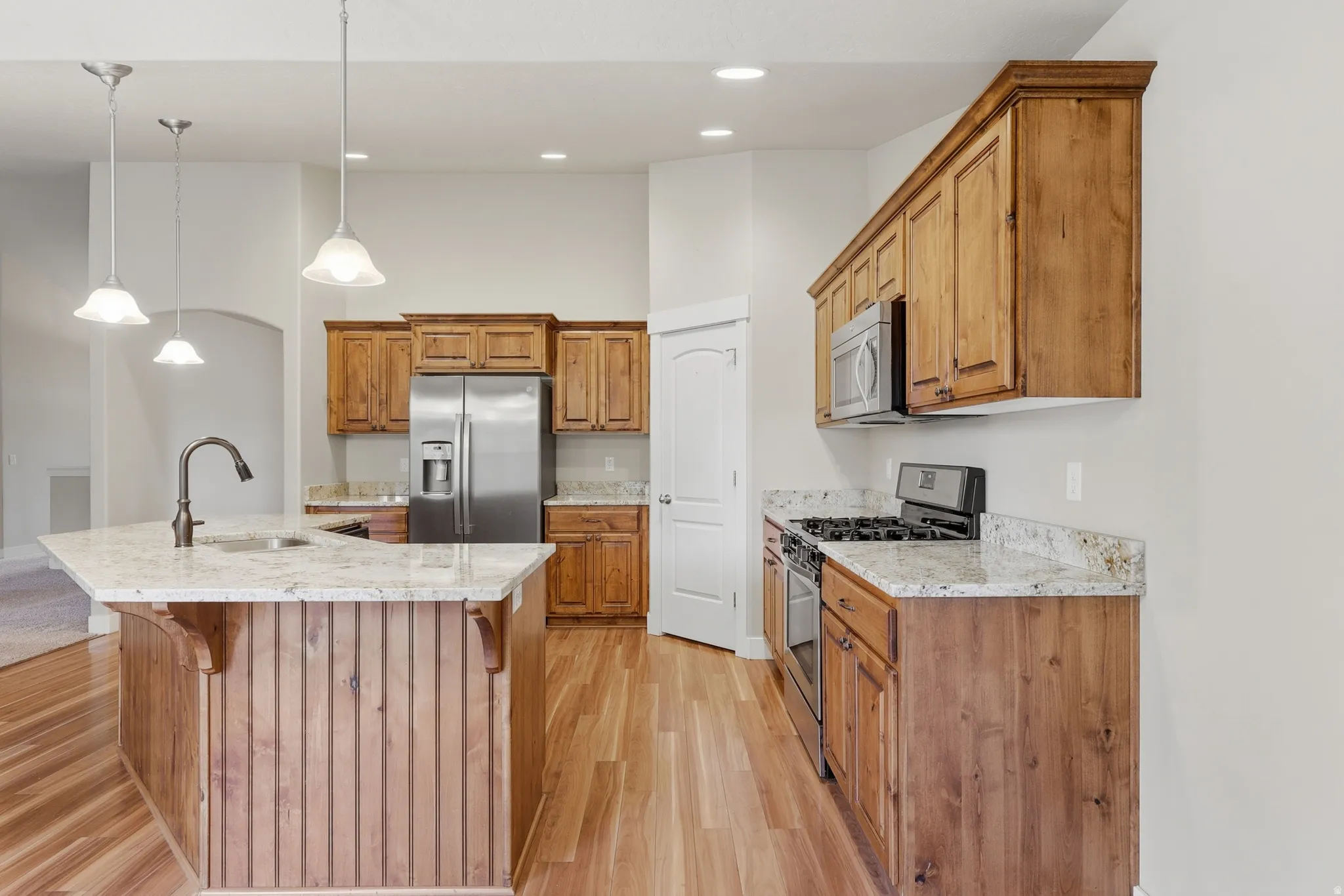 Gourmet kitchen featuring a central island with integrated sink, custom Alder cabinetry, stainless steel appliances, granite countertops, and hardwood flooring.